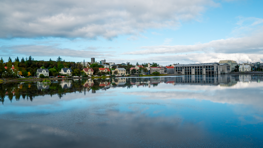 Reykjavik's central lake, Tjornin, reflecting city residences' and surrounding trees' beneath a clear blue sky.