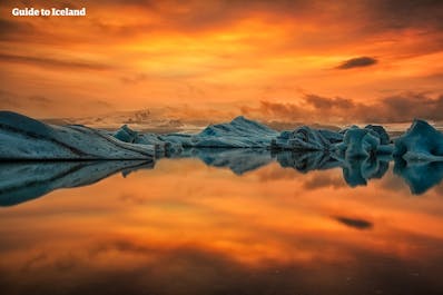 De vurig gekleurde winteravondhemel van IJsland wordt weerspiegeld in het oppervlak van de gletsjerlagune Jökulsárlón en vormt een spectaculair contrast met de azuurblauwe ijsbergen.