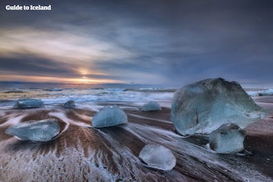 남동부 아이슬란드의 마법같은 곳 중 하나는 푸른 빙산이 검은 모래 위에 놓여 있으며 소용돌이 치는 하얀 파도와 아름답게 대조되는 다이아몬드 해변입니다.