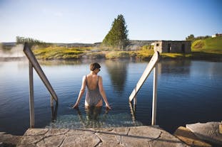 A person in a swimsuit walks down steps into the geothermal waters at the Secret Lagoon spa.
