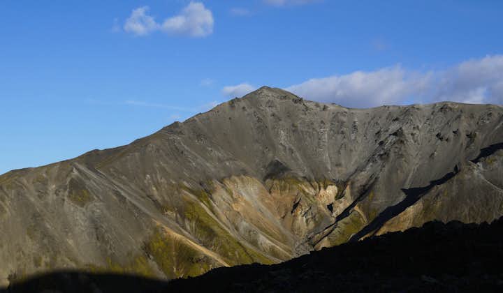 A close-up view of a mountain peak on the Laugavegur trail in the Icelandic Highlands on a cloudy-blue sky summer day.