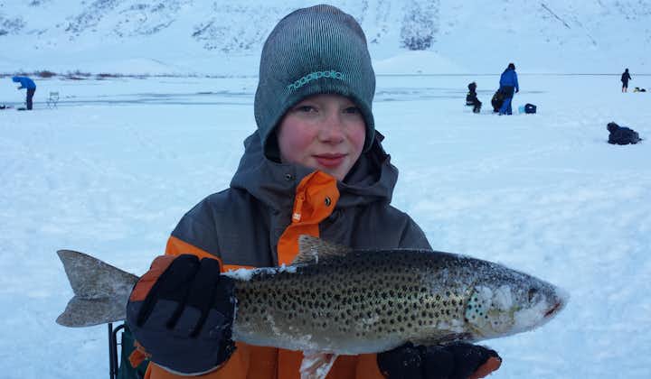An ice fishing tour participant posing with a huge trout.