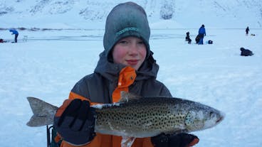 An ice fishing tour participant posing with a huge trout.