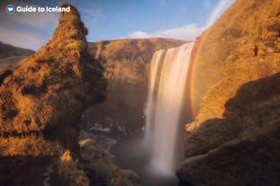 Skogafoss looks spectacular with its rugged natural surroundings bathed in the sun's orange glow.