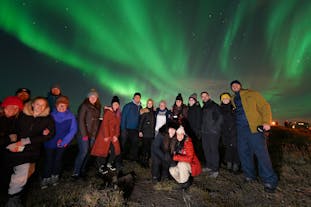 A group of people pose for a photo under the northern lights in Iceland.