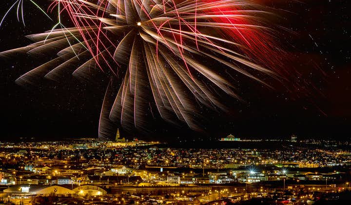 View of Reykjavik’s city lights with an impressive New Year’s Eve fireworks display lighting up the starry midnight sky above.