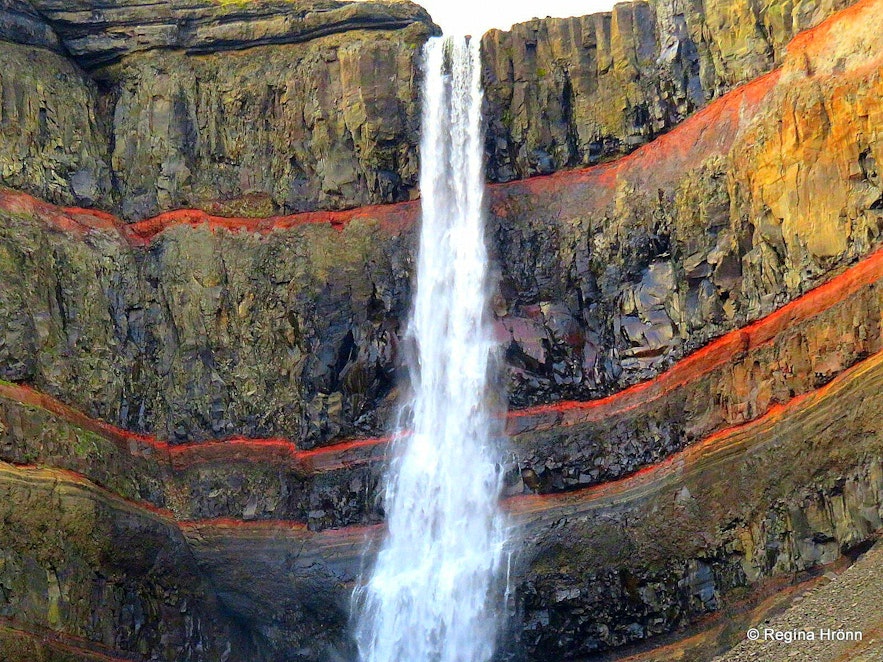 Det er en vakker rødfarge i steinene bak vannfallet Hengifoss på Øst-Island