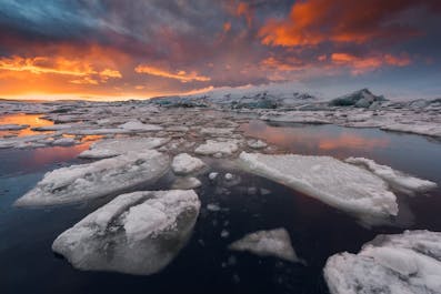 Great icebergs break from Breiðamerkurjökull glacier, falling into Jökulsárlón glacier lagoon to tranquilly drift towards the open sea.