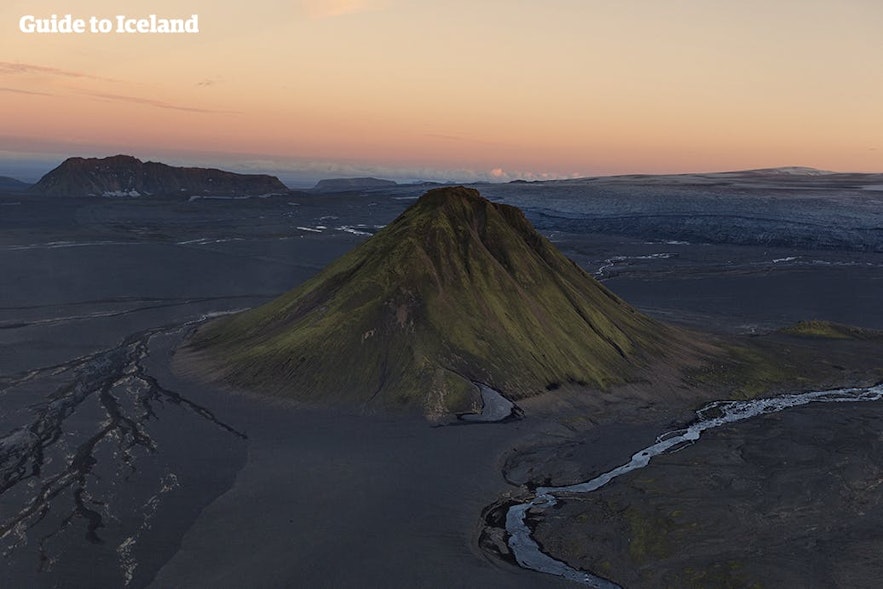 Et frittstående fjell omgitt av svart sand i Islands høyland