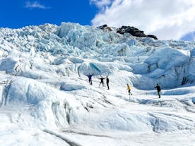 A group of people are standing on a glacier in Skaftafell, Iceland, wearing crampons and helmets for safety.