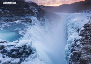 Gullfoss vattenfall på vintern avger vattenstänk som fryser på klipporna och mossan runt det, vilket skapar en dramatisk vinterkuliss.