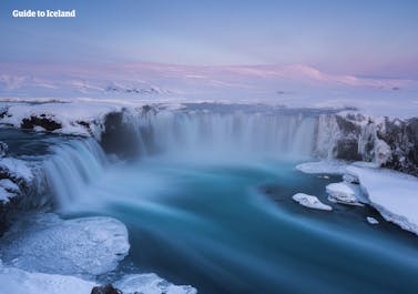 Nella luce rosa di un basso sole invernale, la cascata di Godafoss contrasta con gli elementi gelidi e continua a scorrere attraverso i paesaggi innevati dell'Islanda settentrionale.
