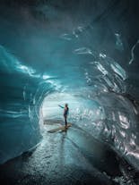 A woman is standing inside the Ice Cave from Katla wearing a waterproof coat and helmet.