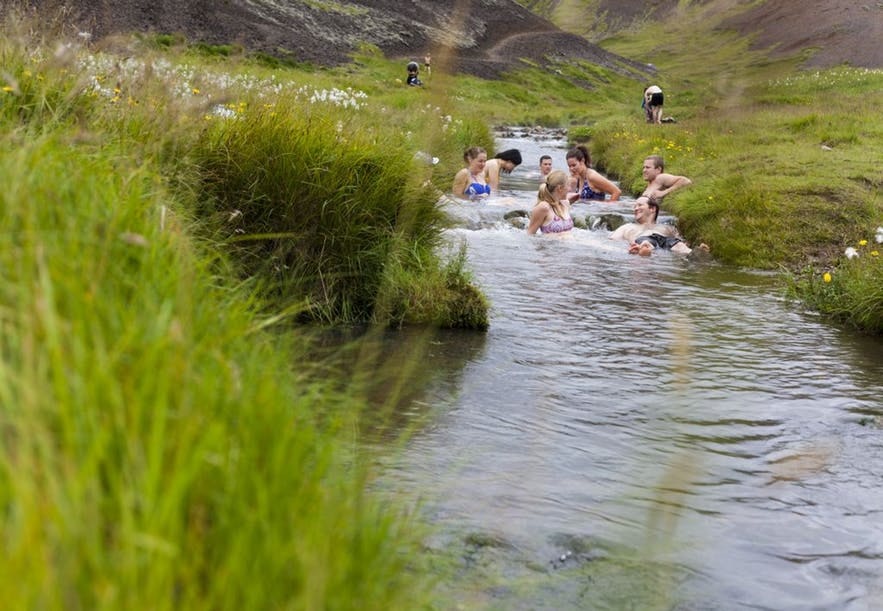 Rejsende hygger sig i en flod med varme kilder i Reykjadalur