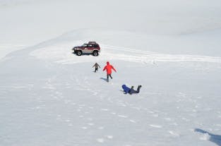 Three people running to a super jeep in the snow, one has fallen face down.