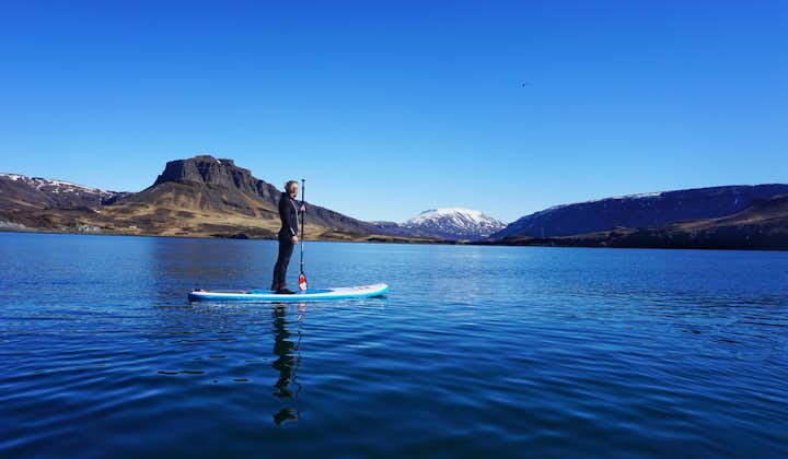 See blue mountains in the distance as you stand on a paddleboard on Hvalfjörður fjord.