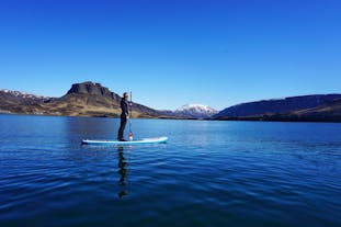 See blue mountains in the distance as you stand on a paddleboard on Hvalfjörður fjord.