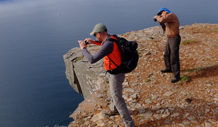 People stand close to a rocky cliff edge and take photos of the water below at the Hornstrandir Nature Reserve in the Westfjords.