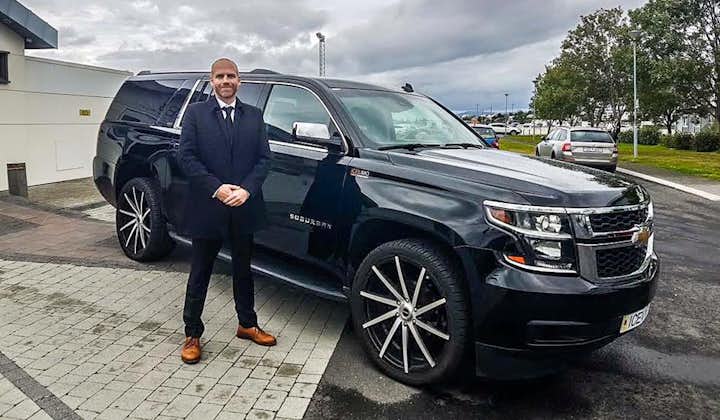 A professional chauffeur wearing a suit stands outside a luxury SUV.