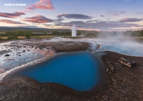 The geyser Strokkur in front of azure coloured fumaroles in the geothermal valley Haukadalur in South Iceland.