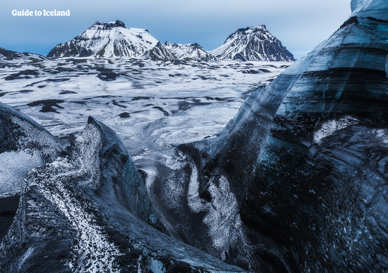 Mýrdalsgjökull's glacier peaks are covered in black ash from past volcanic eruptions.