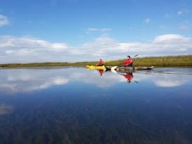 Två äventyrare som paddlar kajak på en lugn sommardag på floderna på södra Island.