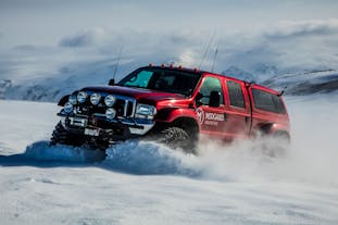 A red, Midgard super jeep plows through the snow-covered landscape on Eyjafjallajokull glacier volcano on a cloudy day.