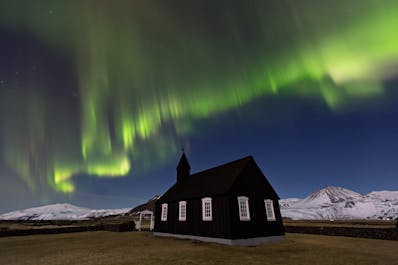 Northern Lights dance across the sky behind the charming black church on the Snæfellsnes Peninsula.