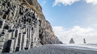 Der Strand Reynisfjara mit schwarzem Sand und Basaltsäulen an einem sonnigen Tag.