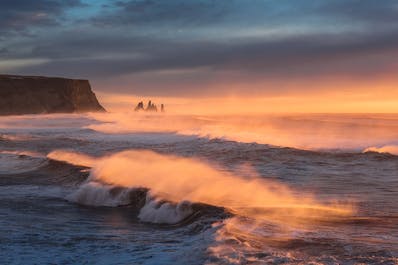 I faraglioni Reynisdrangar in lontananza, mentre le onde si infrangono sulla riva.