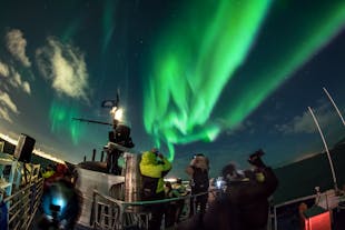 A group of people admiring and taking pictures of the northern lights from a boat.