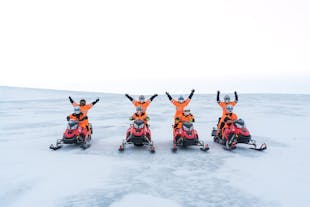 A group of people on snowmobiles on the Langjokull glacier raise their hands above their heads.