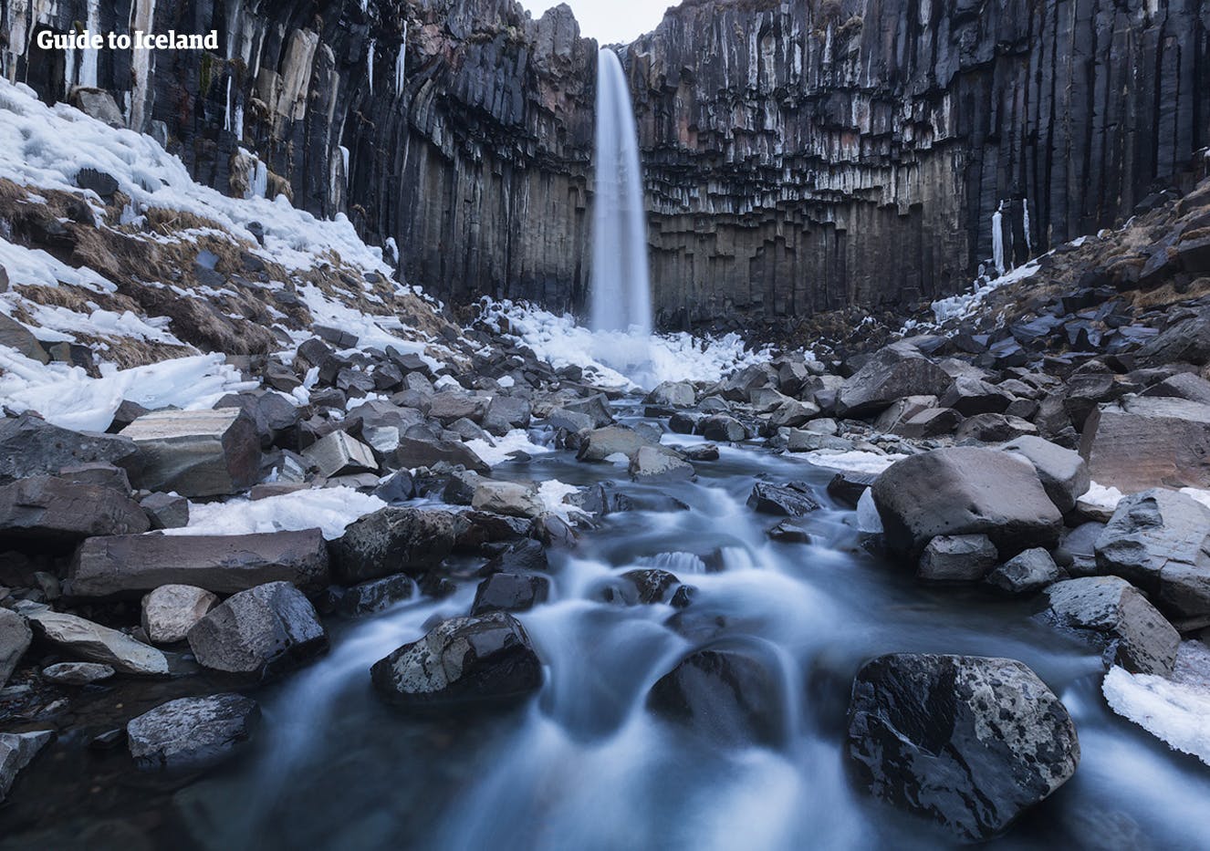 Sześciokątne czarne kolumny otaczają wodospad Svartifoss w południowej Islandii, przedstawiony tutaj zimą.