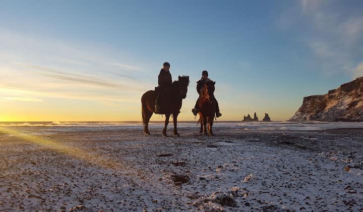 Cavalieri sulla spiaggia di Reynisfjara all'inizio dell'inverno, con Reynisdrangar sullo sfondo. Vík, Islanda meridionale.