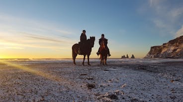 Reiter am schwarzen Strand bei Vík im frühen Winter, mit Reynisdrangar im Hintergrund.