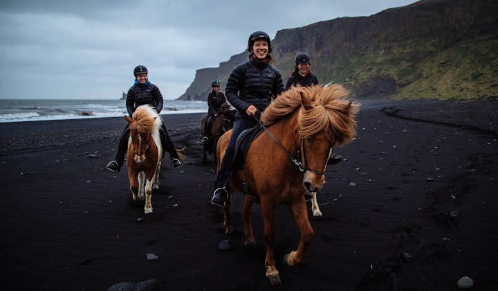 Un cavallo rosso con un cavaliere sorridente, in un gruppo che si allena nel tölt sulla sabbia. Vík, Islanda meridionale.