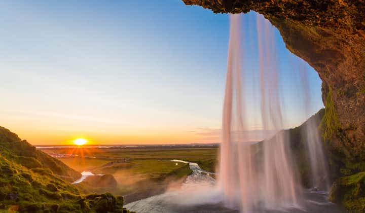 The sun hangs low in the sky in front of majestic Seljalandsfoss waterfall in Iceland.