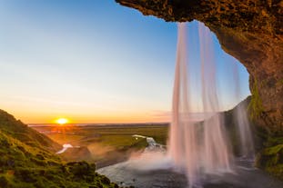 The sun hangs low in the sky in front of majestic Seljalandsfoss waterfall in Iceland.