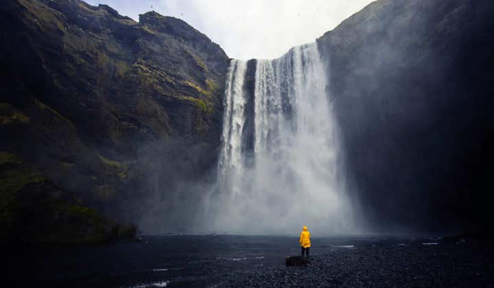 Person wearing raincoat stands at the bottom of a magnificent waterfall in Iceland.