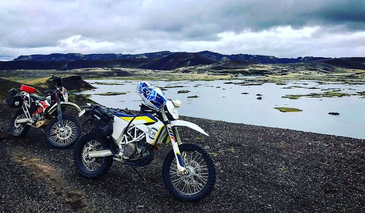 A husky motorcycle resting at a highland lake with moss covered mountains in the background.