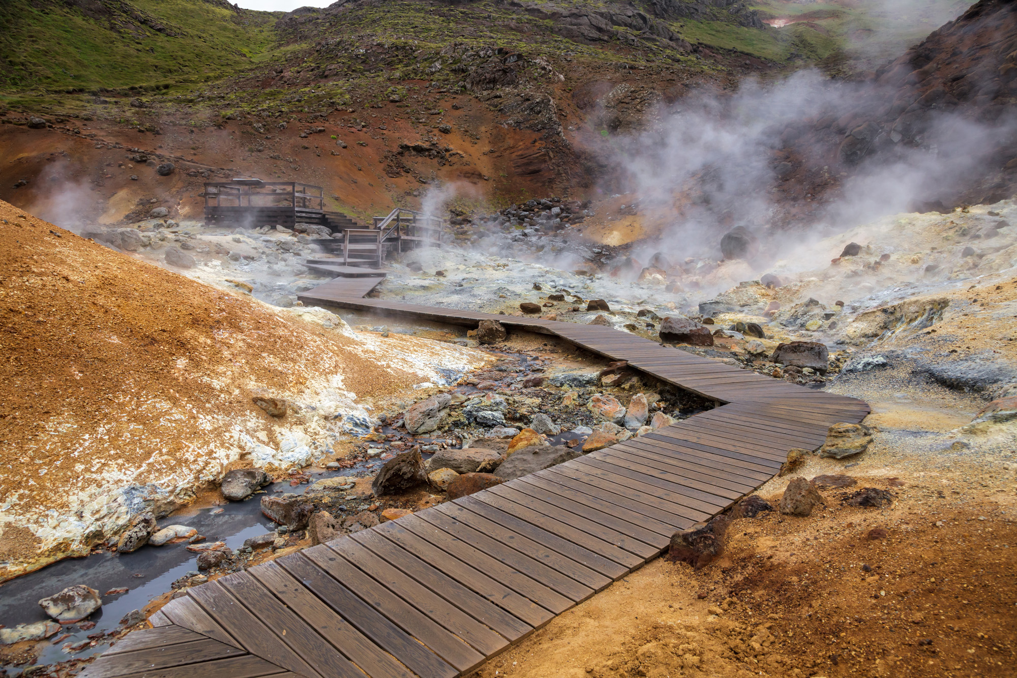 Steam rises from the ground amid wooden walkways in the Seltún geothermal area