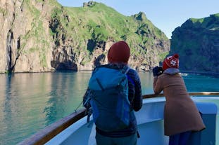 Two people on a boat looking at the cliffs of the Westman Islands.