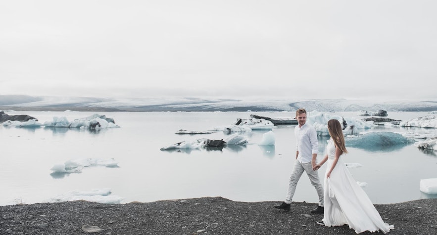 Les jeunes mariés marchent à côté d'une lagune glaciaire dans le sud de l'Islande.