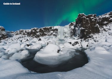 Zorza polarna tańcząca nad wodospadem w Parku Narodowym Þingvellir.
