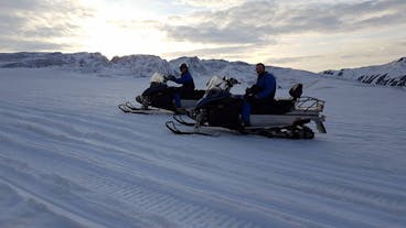 Ett par på sina snöskotrar under midnattssolen på Vatnajökullglaciären.