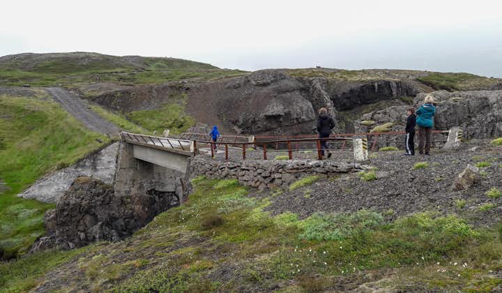 People are walking across a bridge amid a rugged Eastfjords landscape.
