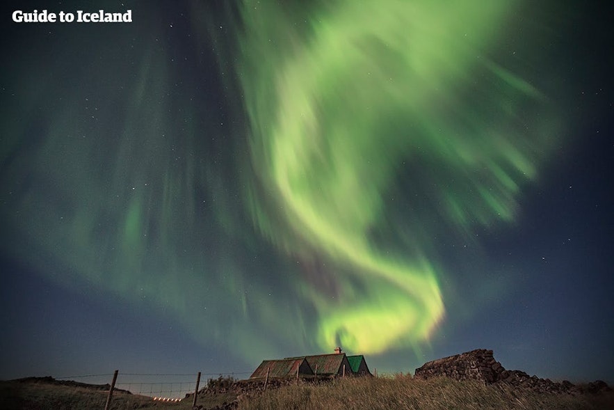 Het noorderlicht dat boven een IJslands huis danst.