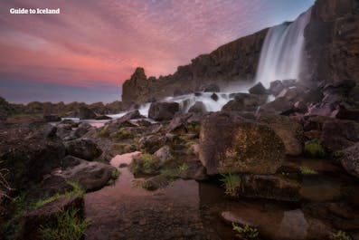 A waterfall in Iceland seen at sunset, with pink and orange hues in the sky.
