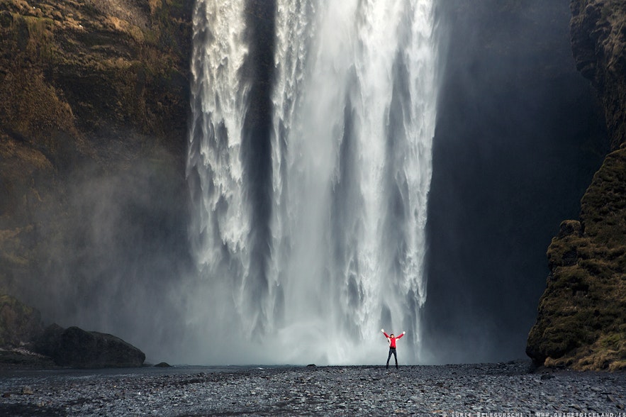 The bottom part of Skogafoss waterfall with a small person in front