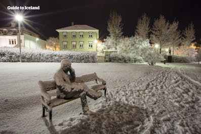 A statue of a man on a bench in a park in Iceland in winter.